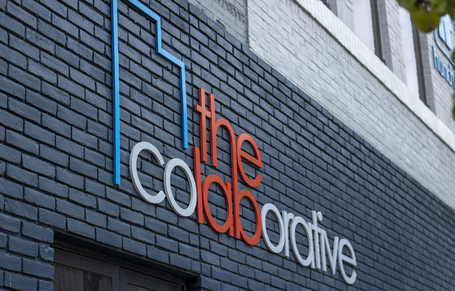 THE coLABorative building exterior with logo signage on dark brick facade